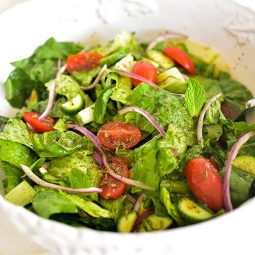 a salad in a white bowl with tomatoes and cucumbers