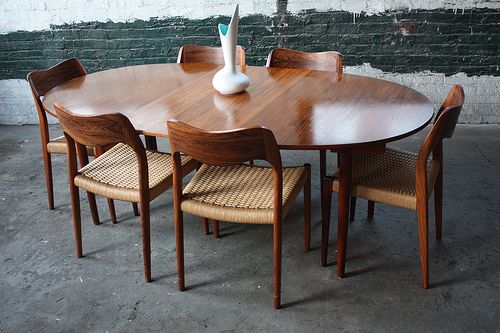 a wooden table with six chairs and a vase on it in front of a brick wall