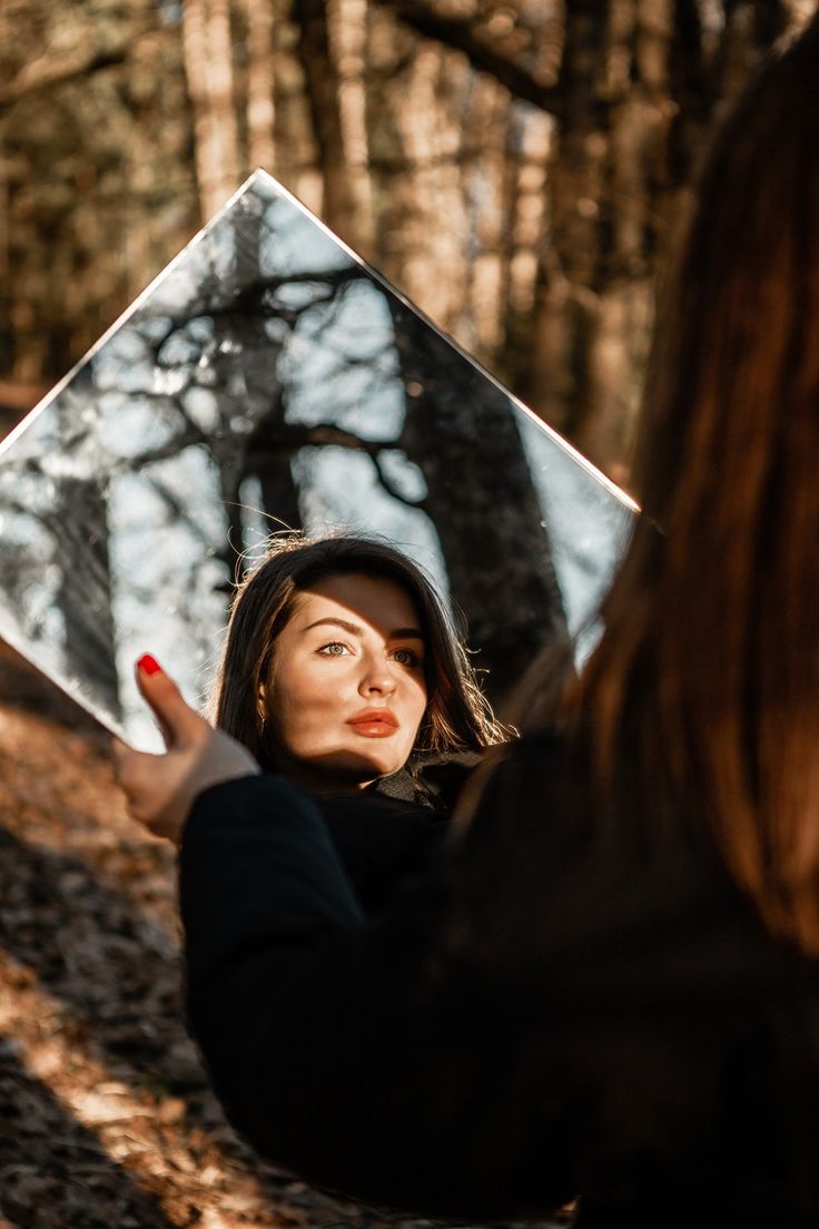 a woman holding up a mirror in the woods