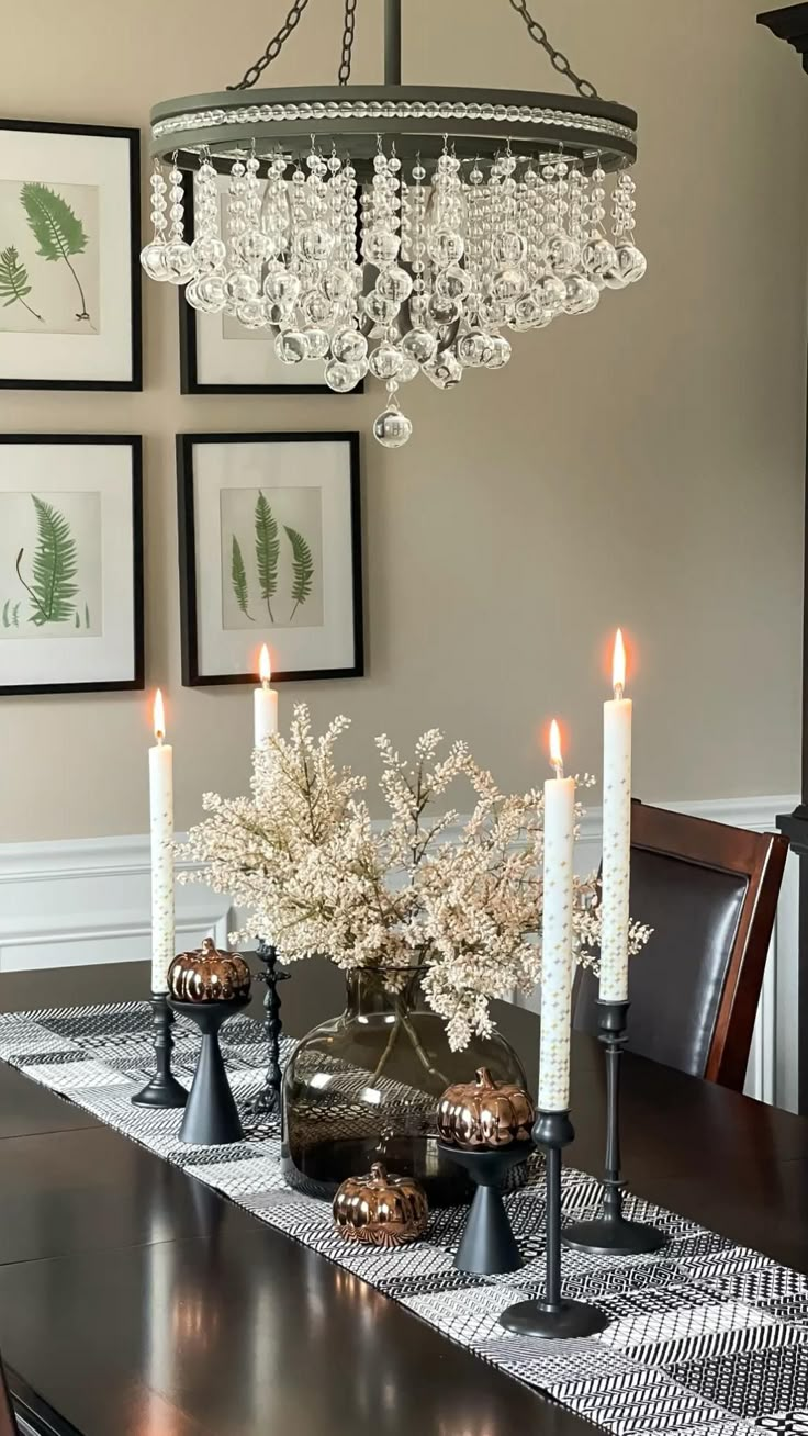 a chandelier hanging over a dining room table with white flowers and candles on it