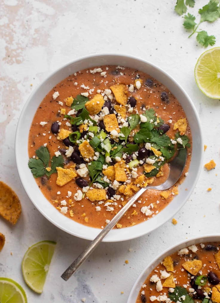 two bowls filled with soup and garnished with cilantro, tortilla chips