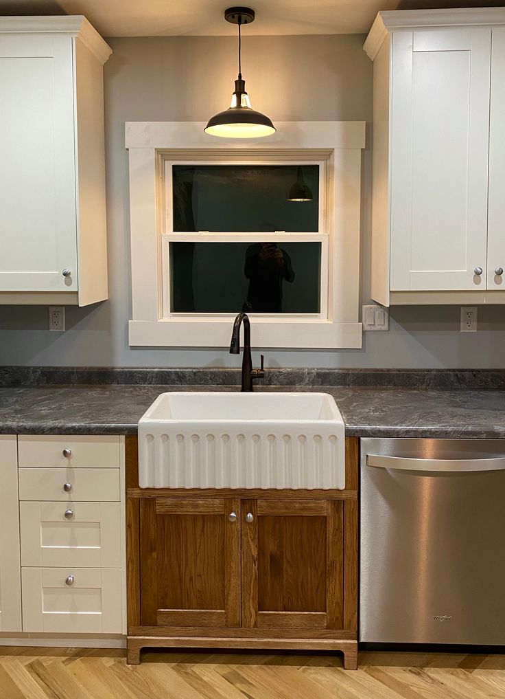 an empty kitchen with white cabinets and wood flooring is pictured in this image, there is a dishwasher on the counter next to the sink