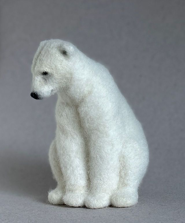 a small white polar bear sitting on top of a gray floor next to a wall