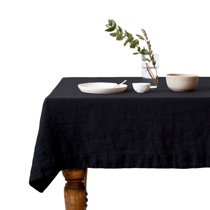 a black table cloth with two bowls and a plant on it, sitting next to each other