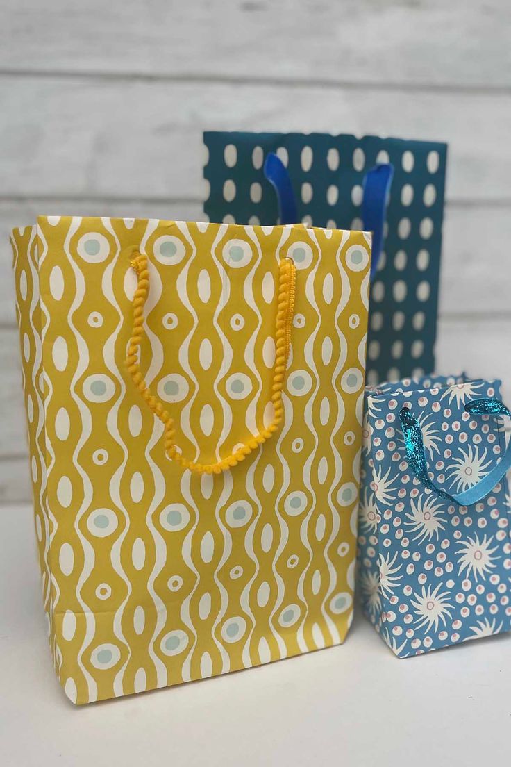 two bags with handles are sitting next to each other on a white table and one has a blue ribbon in it