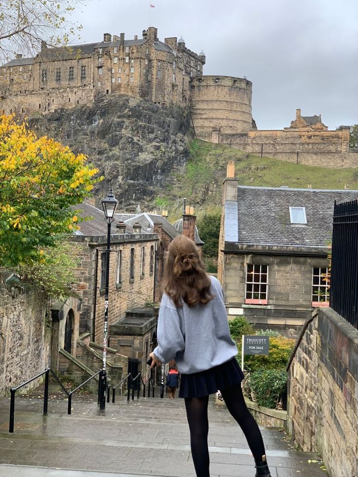 a woman riding a skateboard down a street next to a tall castle on top of a hill