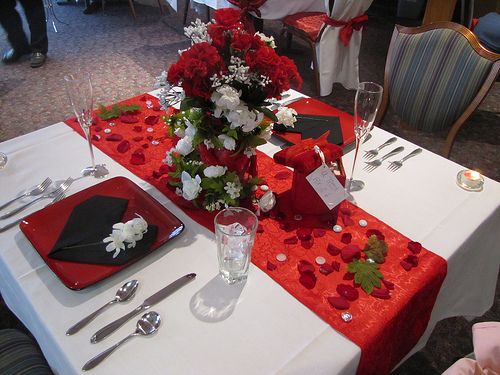 the table is set with red and white flowers, silverware, and napkins