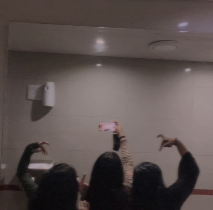 some people in a room with their hands up and one person taking a photo on a cell phone