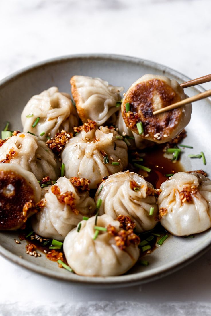 some dumplings are sitting on a plate with chopsticks in it and garnished with seasoning