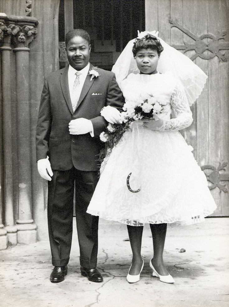 an old black and white photo of a man and woman in wedding attire standing next to each other