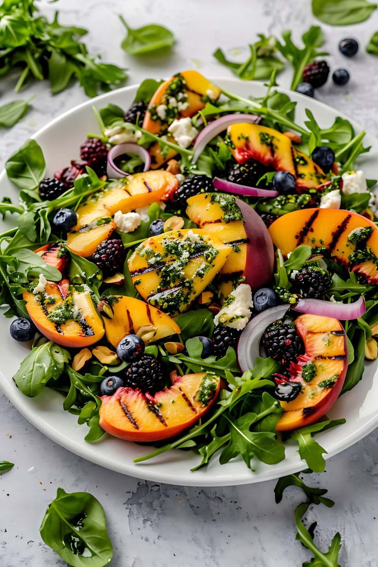 a white plate topped with grilled peaches, blueberries and spinach salad