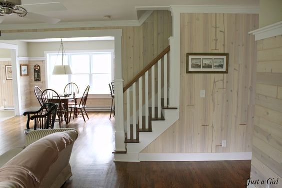 a living room filled with furniture next to a wooden floored staircase leading up to a dining area