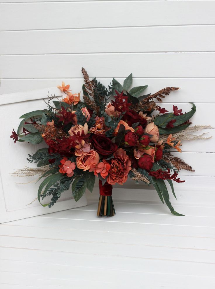 a bouquet of flowers sitting on top of a wooden bench next to a white wall