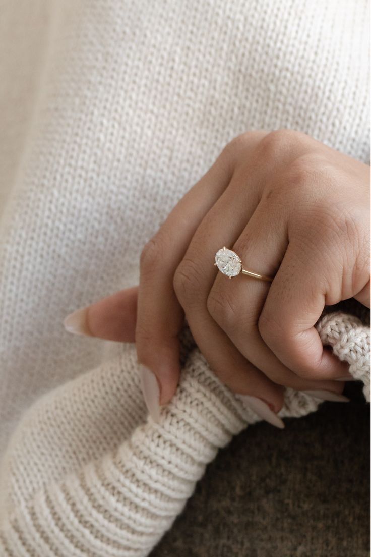 a woman's hand with a diamond ring on her finger, sitting on a white sweater