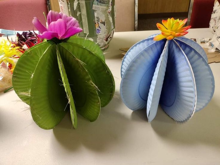 two paper flowers sitting on top of a table next to each other in front of a vase