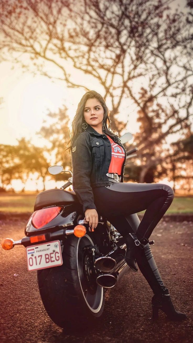 a woman sitting on top of a motorcycle in the middle of a parking lot at sunset