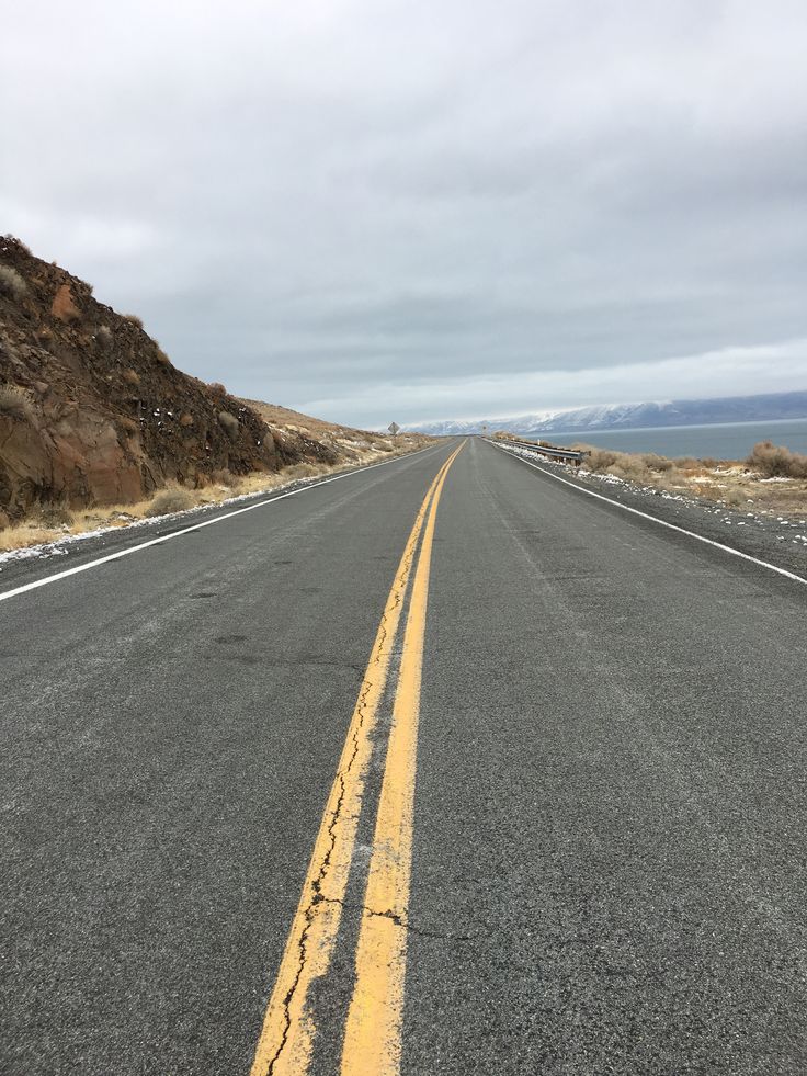 an empty road with yellow painted lines on the side and mountains in the back ground