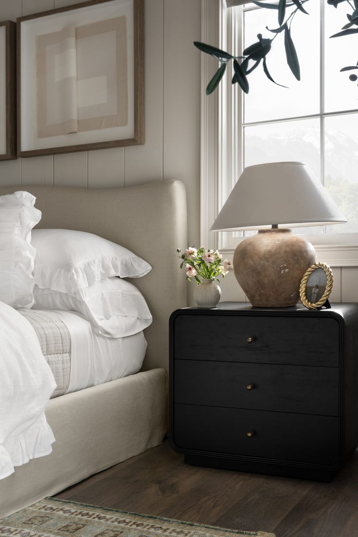 a bed with white sheets and pillows next to a nightstand with a lamp on it