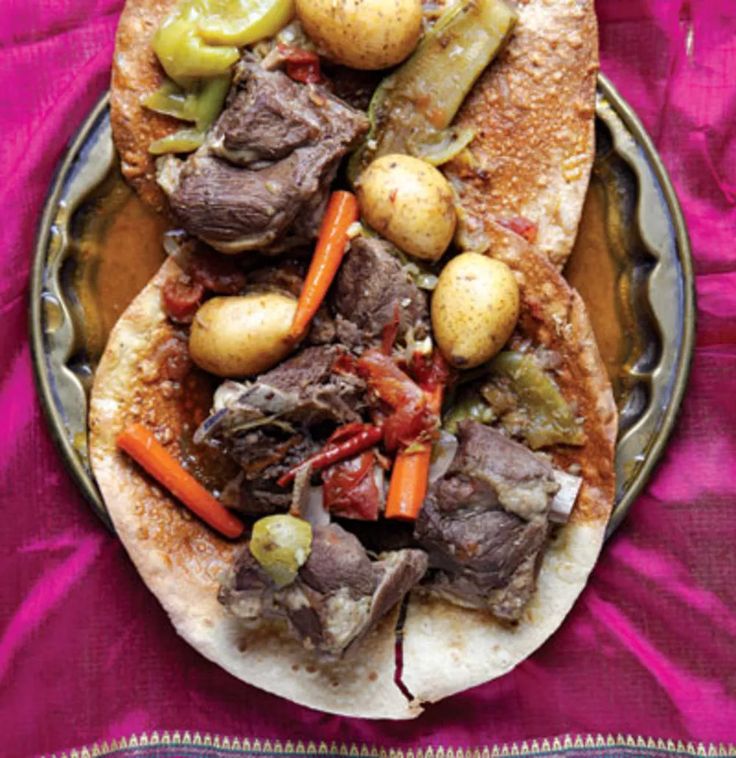 a plate filled with meat, potatoes and carrots on top of a purple cloth