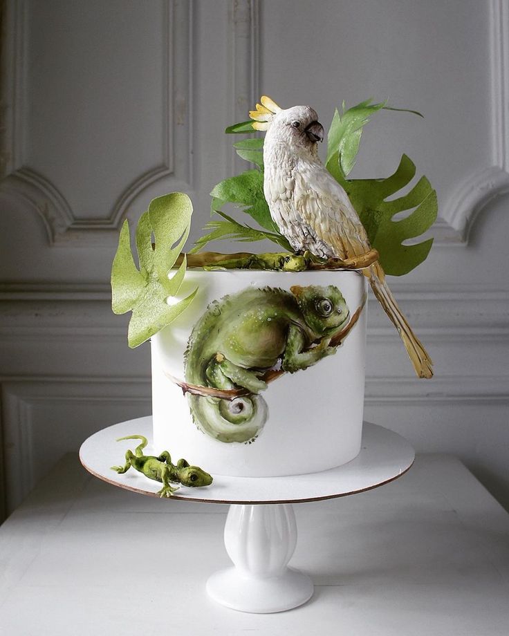 a white cake with green plants and a bird on top