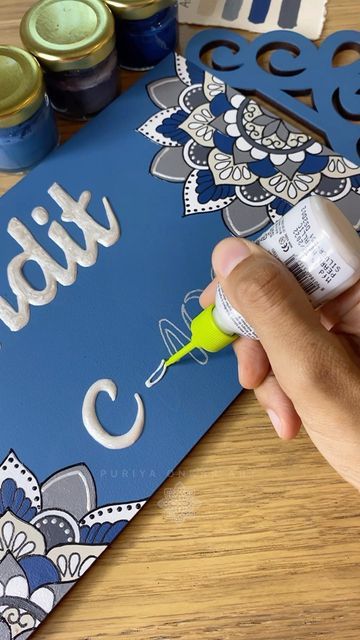 a person is painting the letters on a blue sign with white and yellow paintbrushes