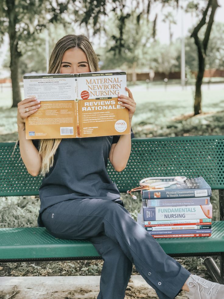 a woman is sitting on a bench reading a book and holding up a copy of the national nursing manual