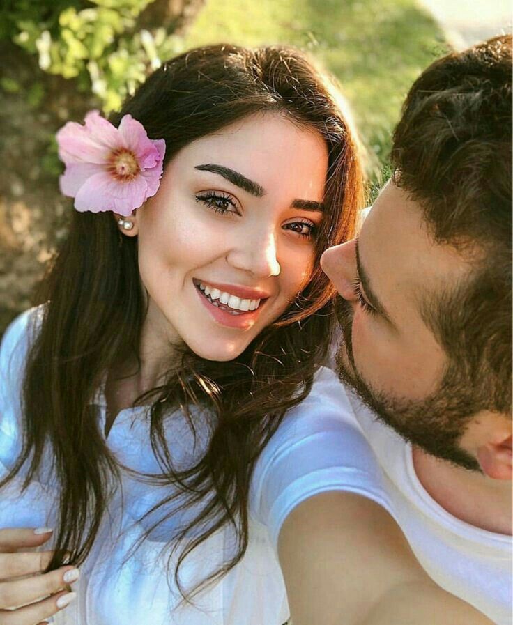 a man and woman smiling at each other with a pink flower in their hair on her forehead