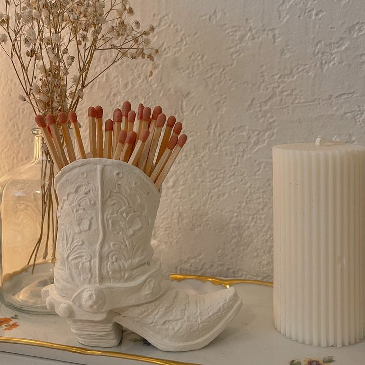 a white vase filled with flowers next to a candle and some candlesticks on top of a table