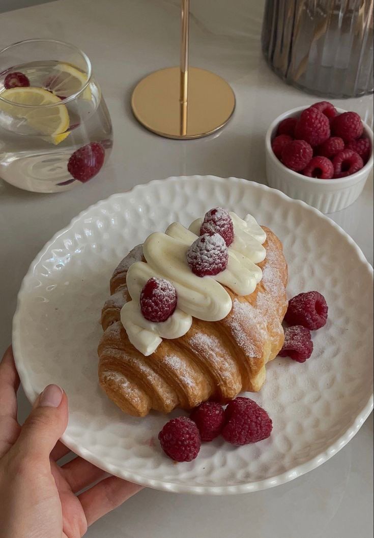 a white plate topped with pastry covered in icing and raspberries on top of a table