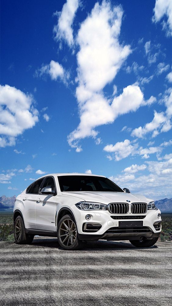 a white bmw suv parked on the side of a road under a cloudy blue sky