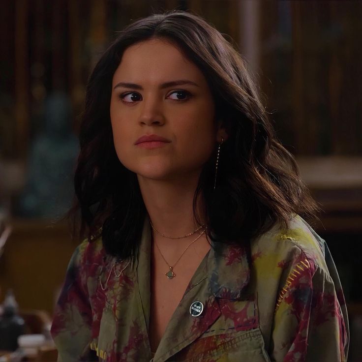 a woman with long dark hair wearing a green shirt and earrings looking at the camera