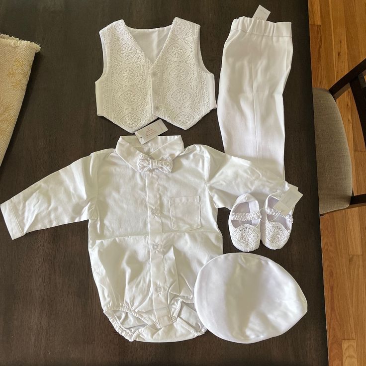 a baby's white outfit and shoes are laid out on the floor