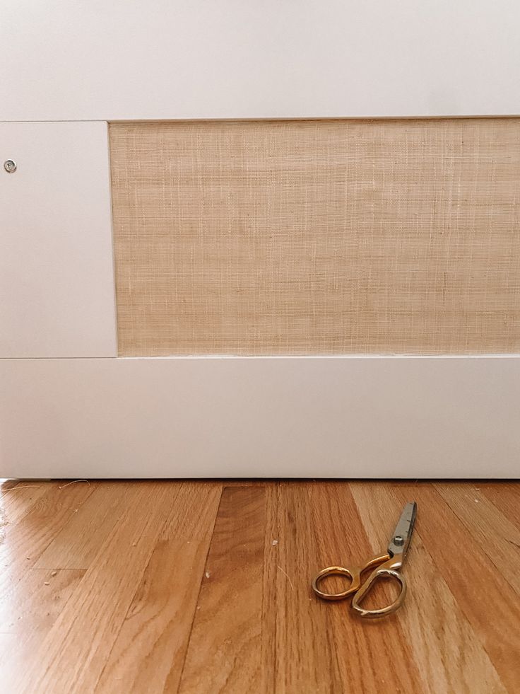 a pair of scissors sitting on top of a hard wood floor next to a wall