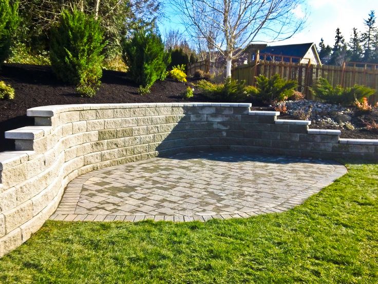 a brick patio with steps leading up to the back yard and landscaping area behind it