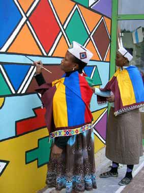 two men in colorful clothing painting on a wall