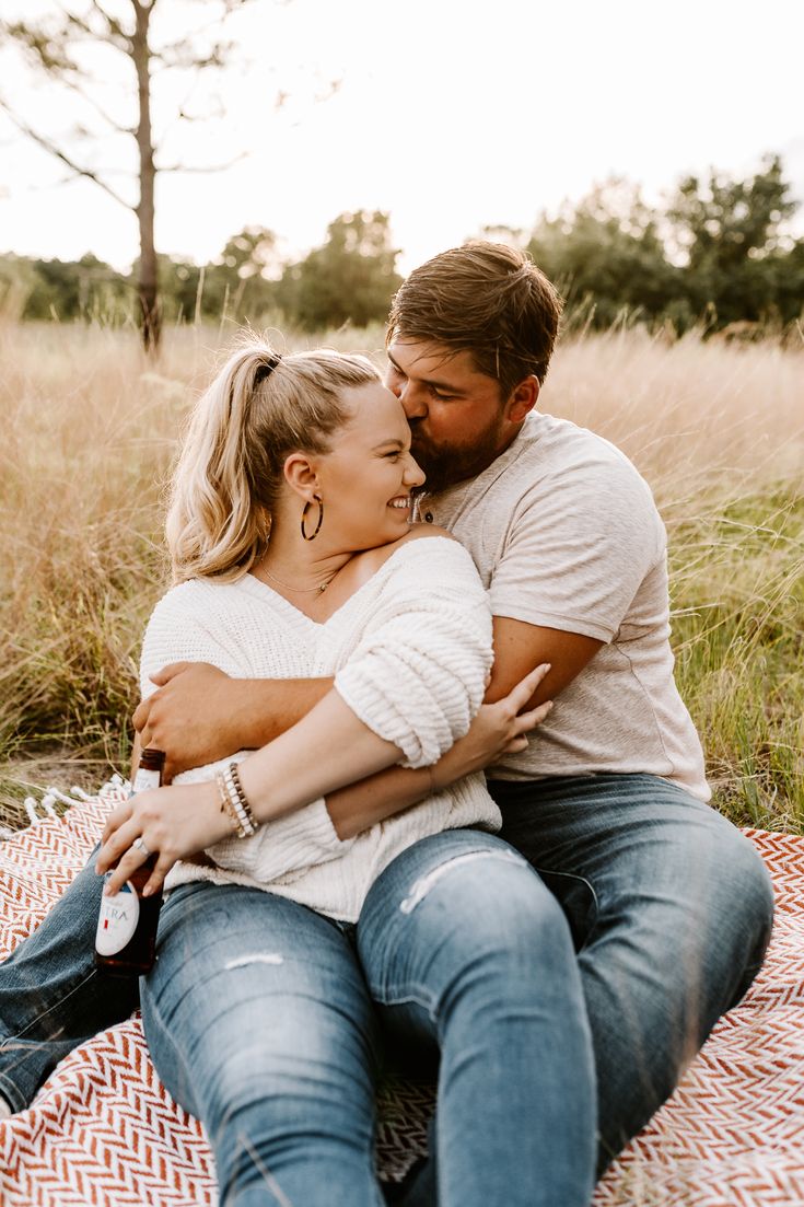 a couple cuddling on a blanket in the middle of a field with tall grass