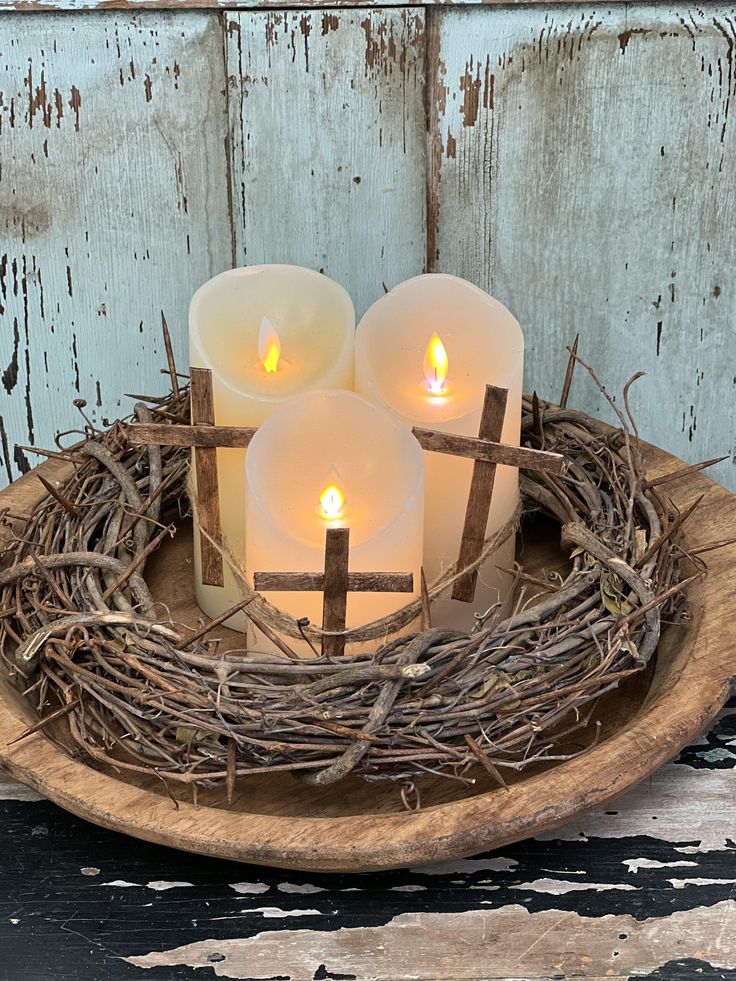 three lit candles in a wooden bowl with twigs on the bottom and one candle between them