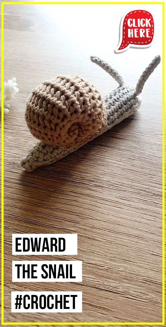 a crocheted snail sitting on top of a wooden table next to a white flower