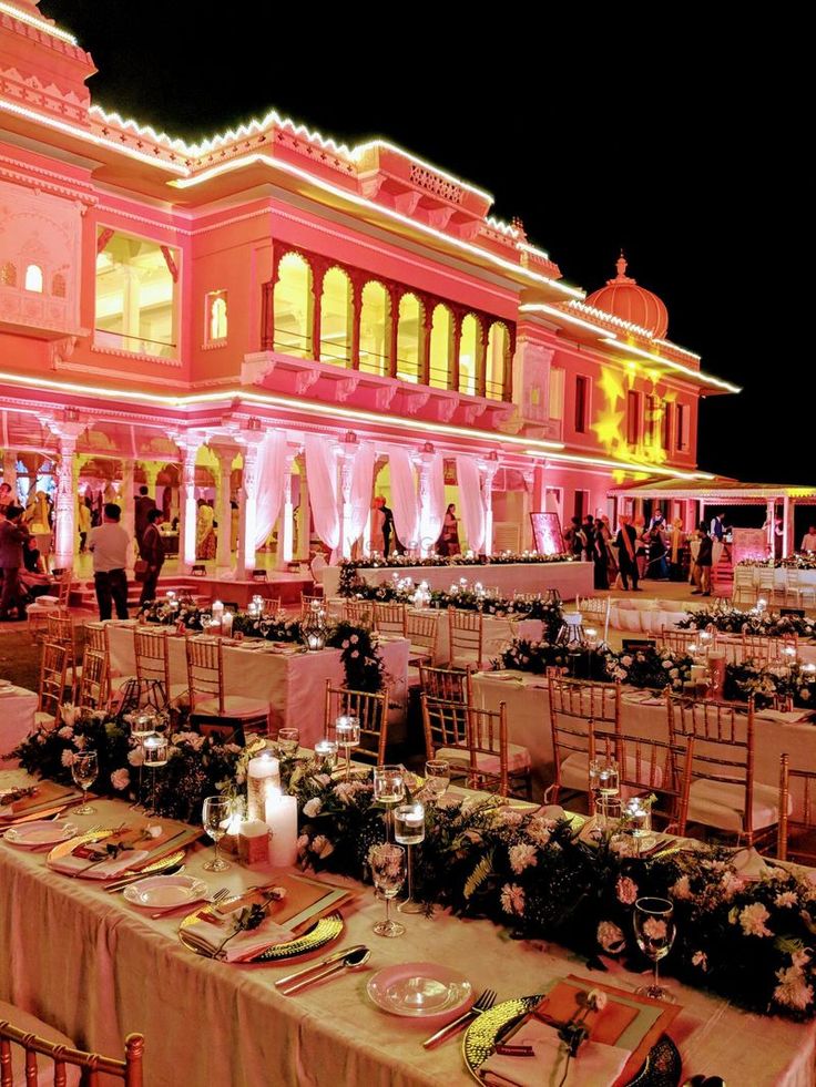 tables and chairs are set up in front of a large building at night with lights on