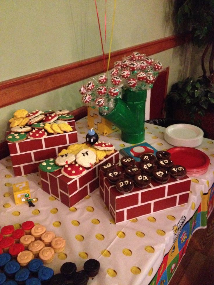 a table topped with boxes filled with cupcakes and cake covered in mario bros decorations