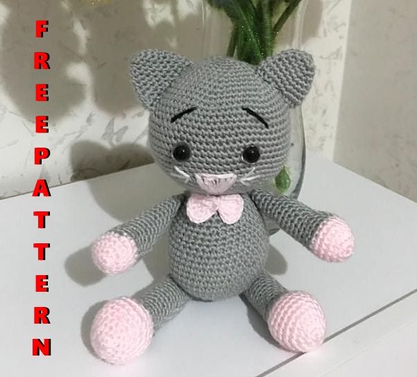 a crocheted cat sitting on top of a table next to a vase with flowers