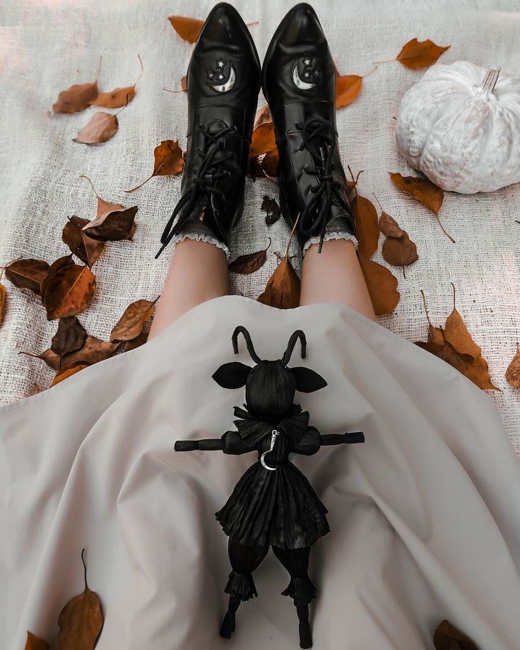 a woman's legs in black shoes and white dress with leaves on the ground