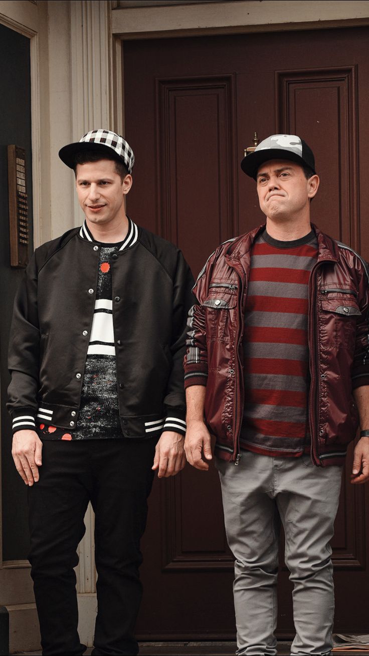 two young men standing next to each other in front of a door wearing jackets and hats