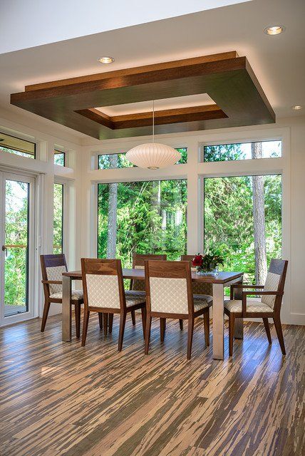 a dining room with wood flooring and large windows overlooking the trees in the woods