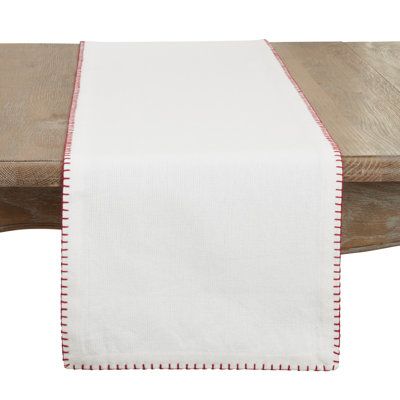 a white table runner with red piping on the edge and a wooden bench behind it