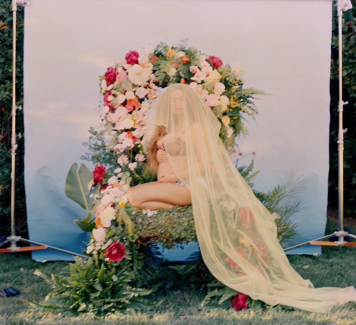 a woman is sitting in front of a floral arch with her veil over her head