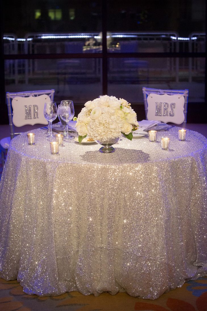 the table is set with white flowers and silver sequins for an elegant centerpiece