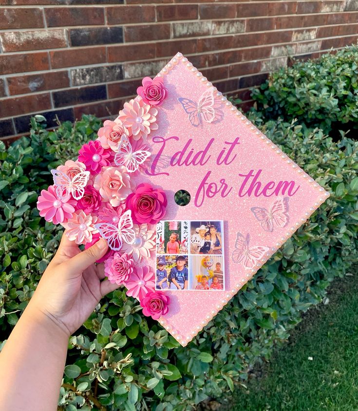 someone holding up a pink graduation cap that says, i did it for them and flowers