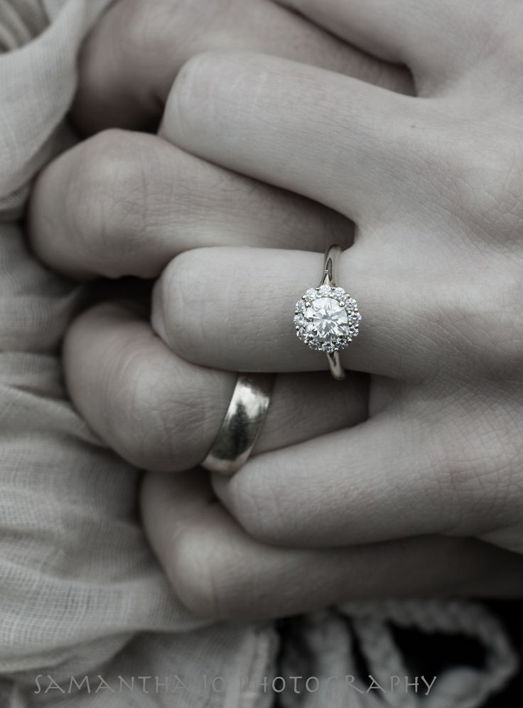 a woman's hand with a ring on top of her finger and the other hand holding an engagement ring