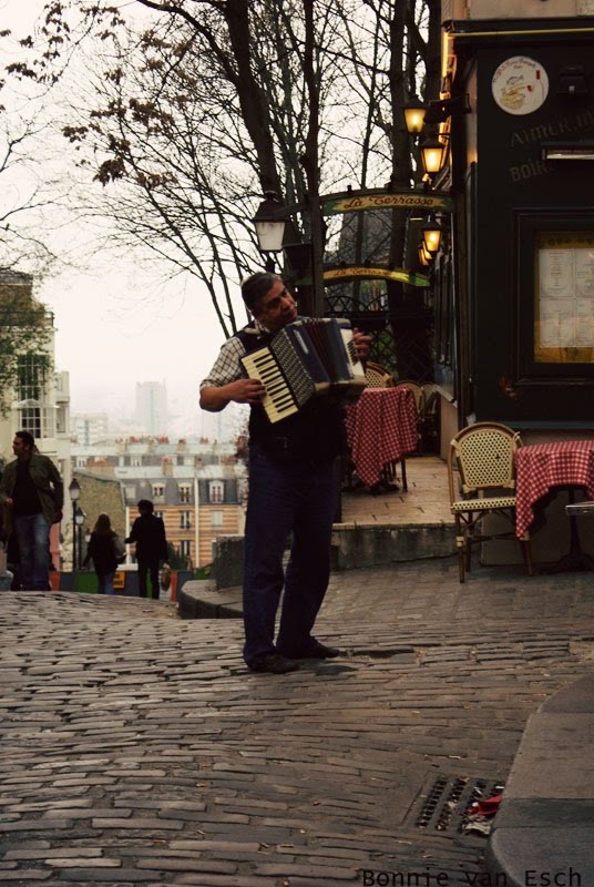 a man is playing an accordion in the middle of a cobblestone street with tables and chairs